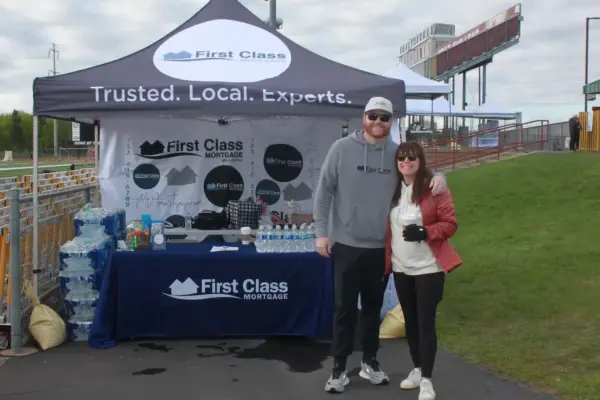 First Class Mortgage representatives at an event booth, showcasing community engagement with a branded table, promotional materials, and smiling attendees.