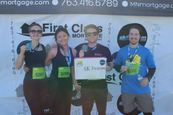Participants celebrating at the First Class Mortgage-sponsored 5K race, holding medals and a "5K Finisher" sign, against a branded backdrop.