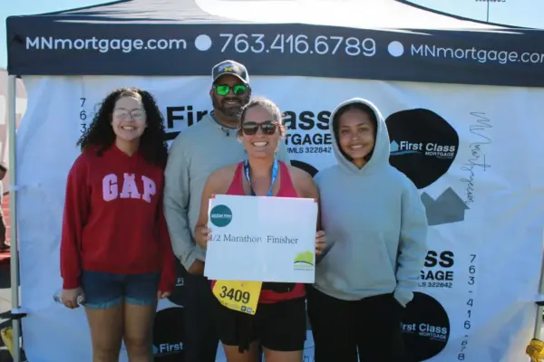 Participants celebrating after the 2026 Maple Grove Lions Half Marathon, showcasing a finisher's medal and a sign, with First Class Mortgage branding in the background.