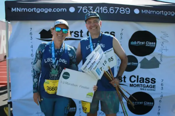 Runners celebrating as half marathon finishers at the First Class Mortgage booth, showcasing medals and a completion sign, highlighting community engagement in local events.